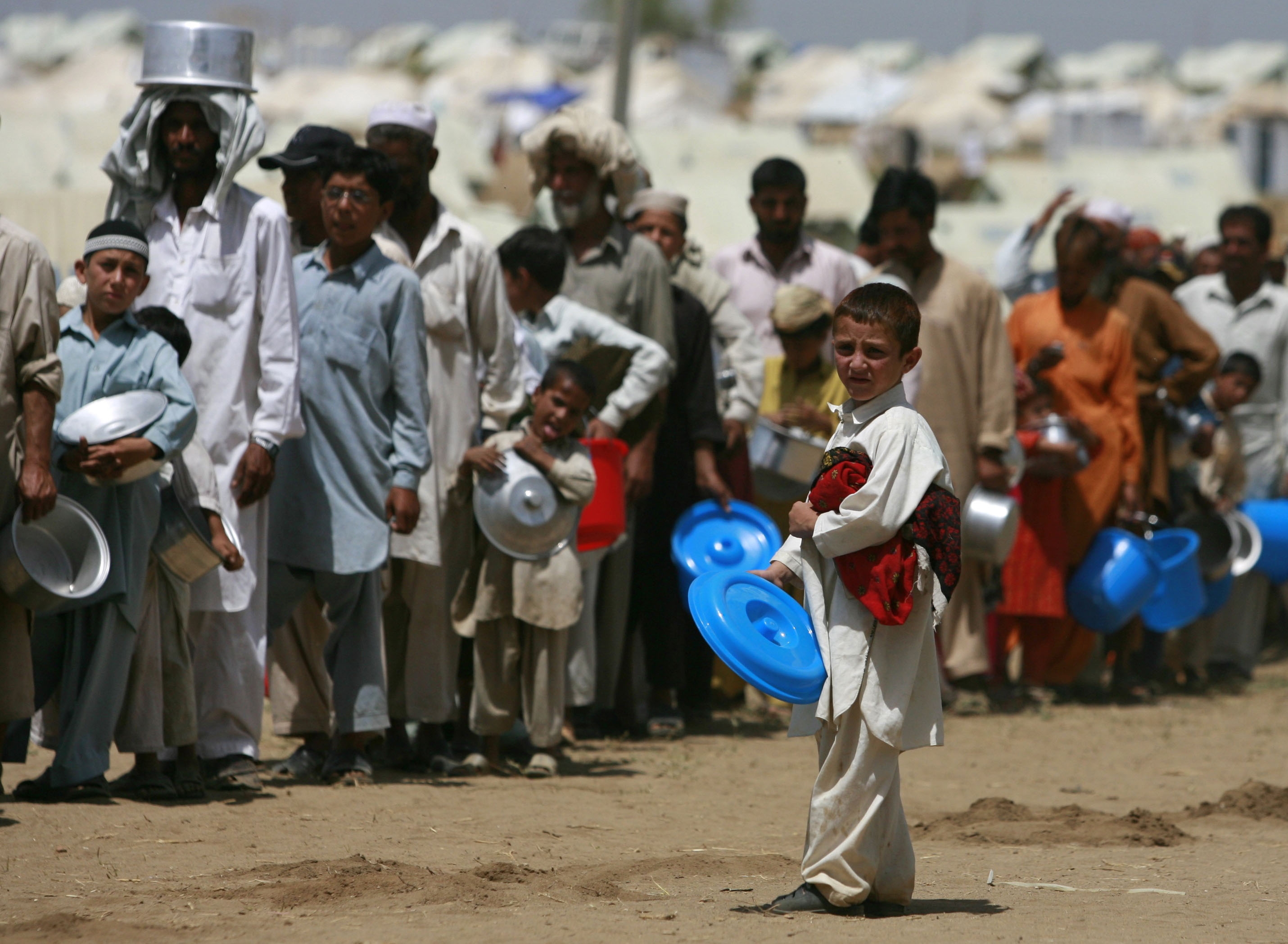 A boy stands near a line of internally displaced people in Pakistan