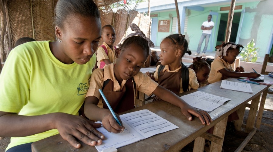 A student practices penmenship with her teacher in Jacmel, Haiti