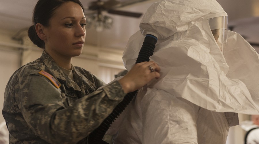 A combat medic helps a student don personal protective equipment during training