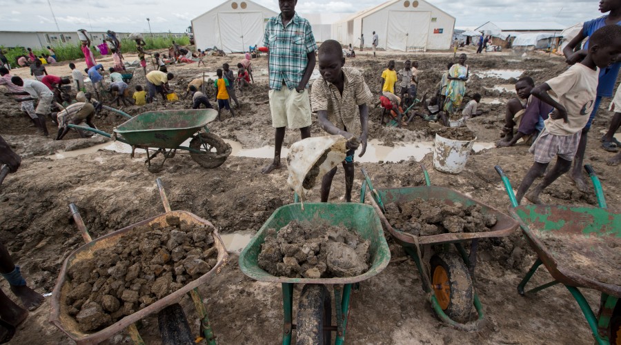 A boy fills wheelbarrows with dirt to build walls in the Protection of Civilians (POC) site near Bentiu, Unity State