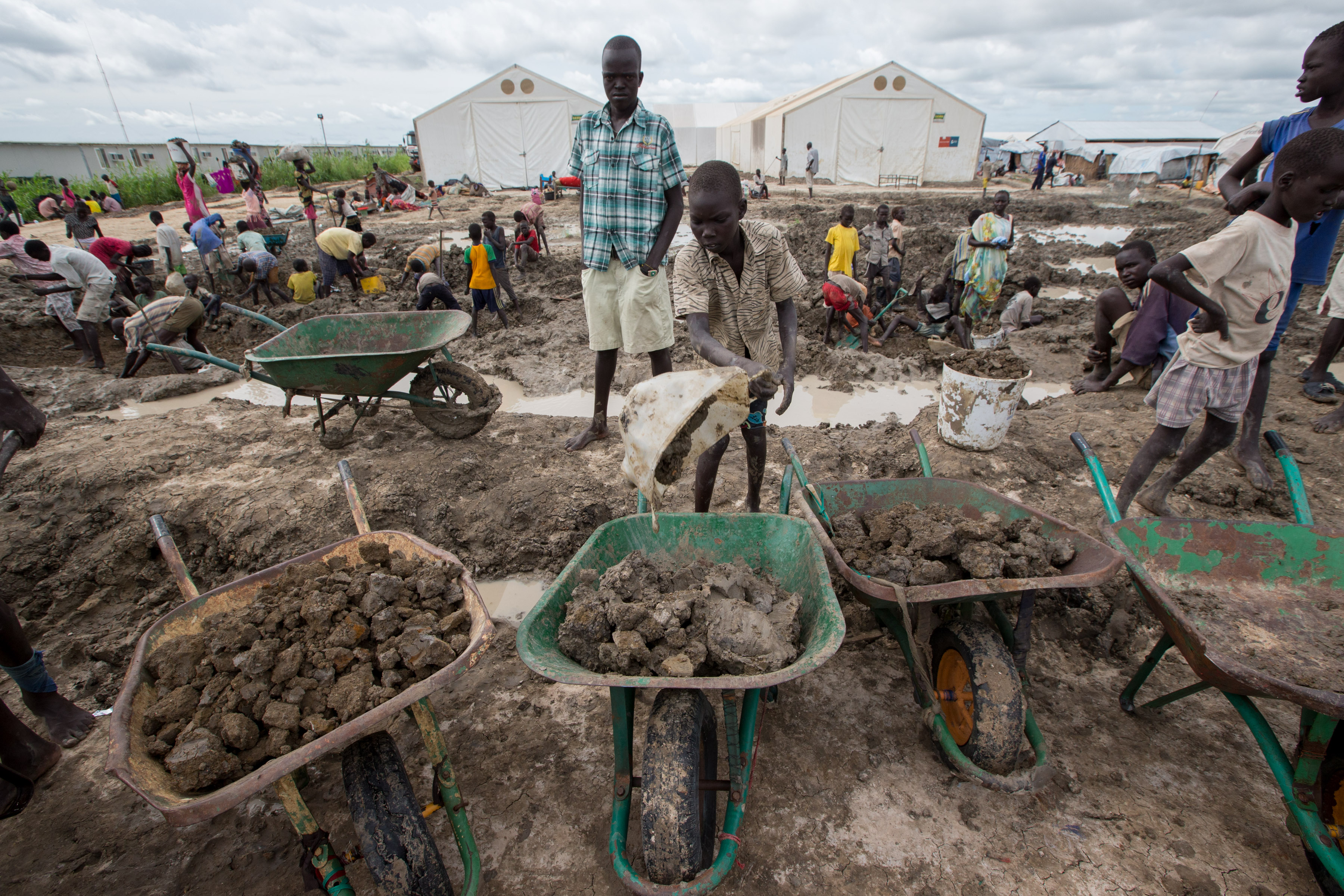 A boy fills wheelbarrows with dirt to build walls in the Protection of Civilians (POC) site near Bentiu, Unity State
