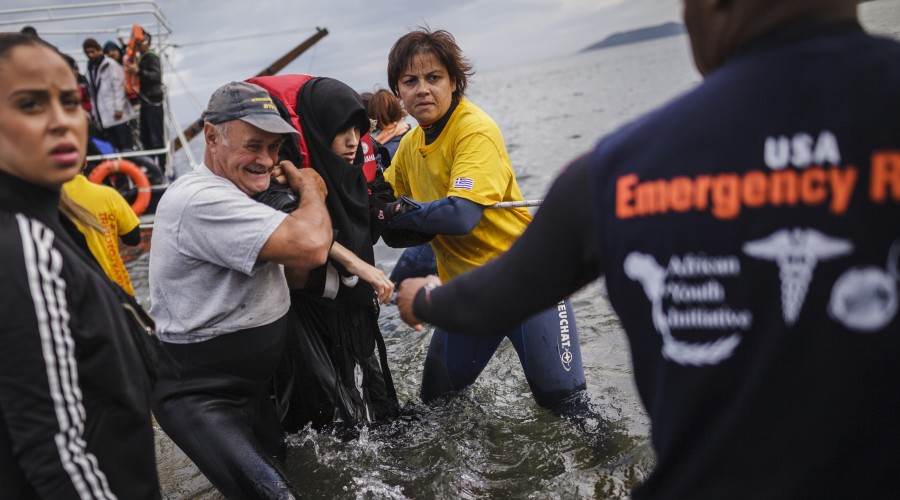 Volunteers help a Syrian refugee ashore on Lesvos, Greece.