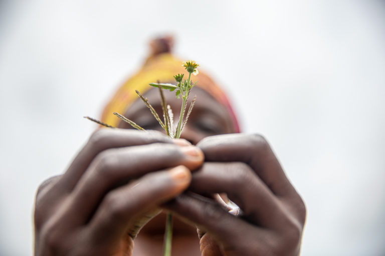 A woman – a survivor of sexual violence – holds a flower to her face in the Elinya site for displaced persons in Democratic Republic of Congo.