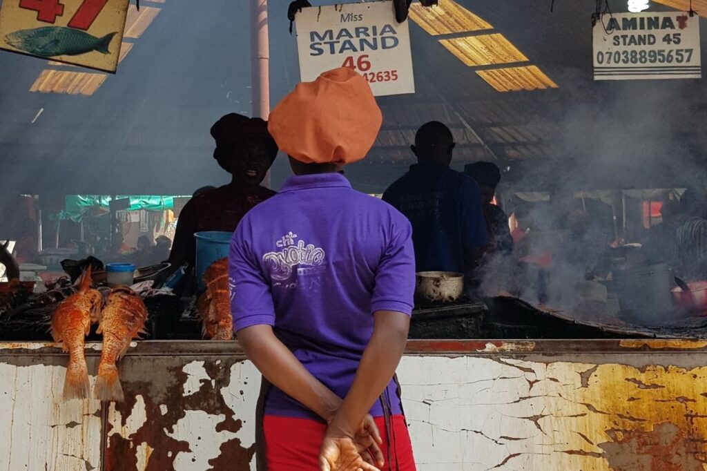 The back of a woman who is standing in front of a fish market stall.