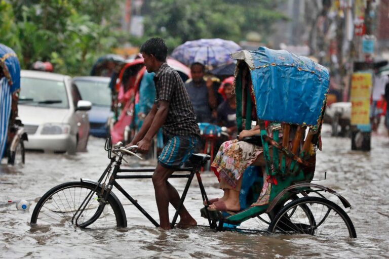 A man struggles to ride his cycle rickshaw through a flooded street.